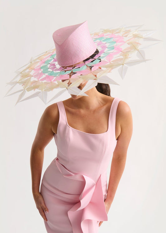 Woman wearing a wide feather brim hat and a pink dress against a white background