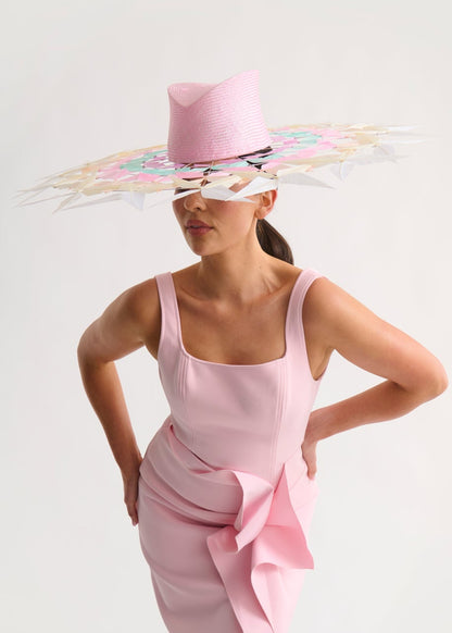 Woman wearing a wide feather brim hat and a pink dress against a white background
