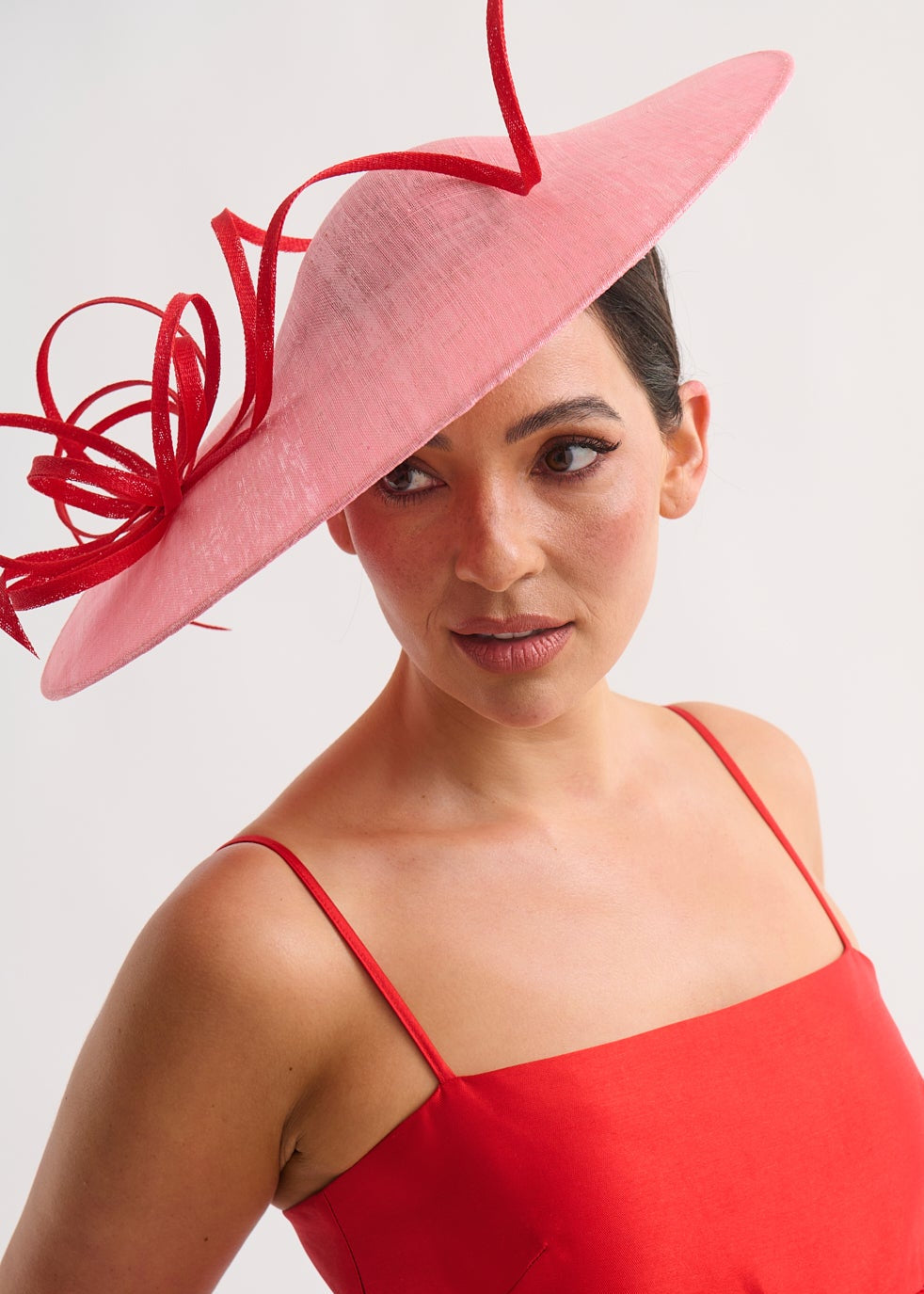 Woman wearing a red dress and large pink hat against a white background