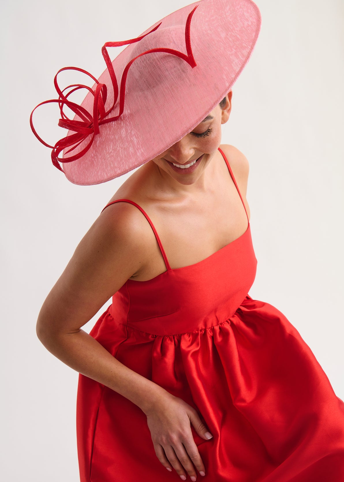 Woman wearing a red dress and large pink hat against a white background