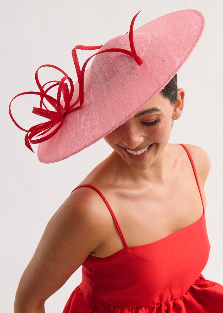 Woman wearing a red dress and pink hat with a decorative bow on a white background