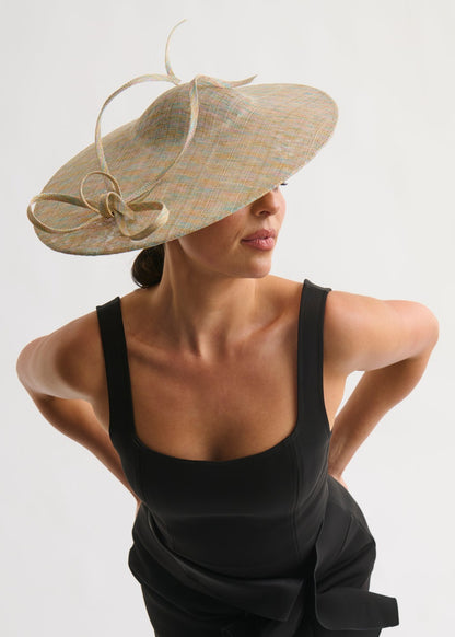 Woman wearing a large decorative hat against a plain background