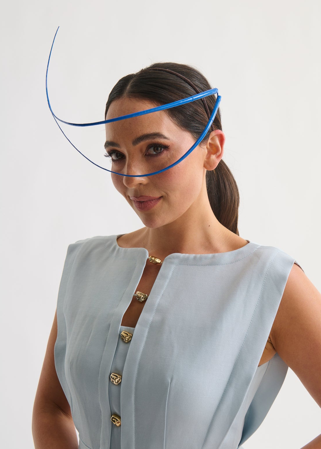 Woman wearing a blue feather quill headpiece and a blue dress against a white background