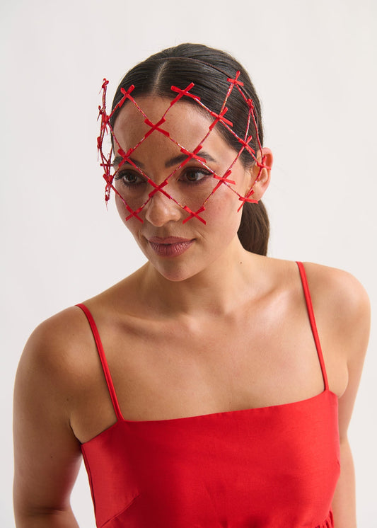 Woman wearing a beaded face veil with small bows and a red dress against a white background