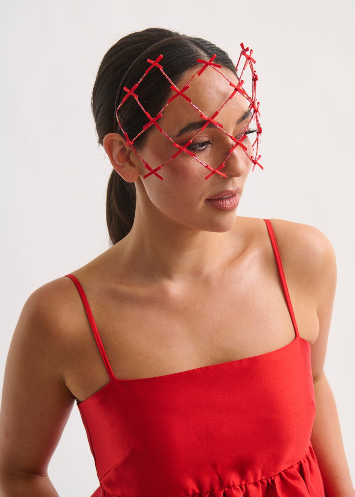 Woman wearing a red dress with a red headpiece against a white background