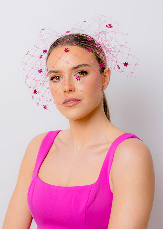Woman wearing a bright pink dress with a decorative headpiece against a plain background