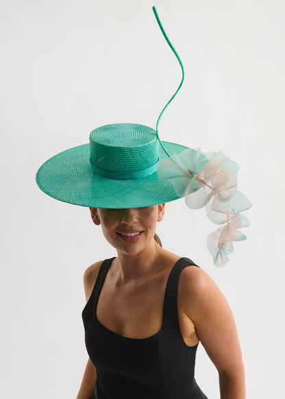 Woman wearing a wide brim hat with ruffle trim and a black dress against a white background