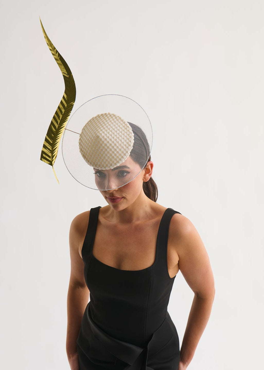 Woman wearing a black dress with a unique headpiece featuring a gold leaf on a white background