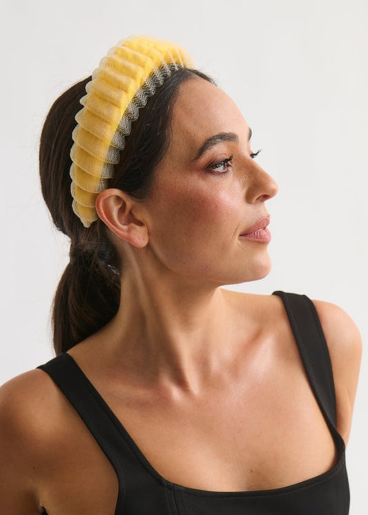 Woman wearing a black sleeveless dress and yellow headband against a white background