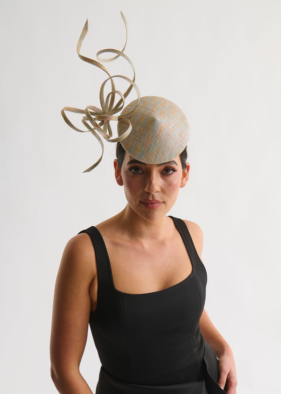 Woman wearing a black dress and a decorative beige hat with intricate design on a white background