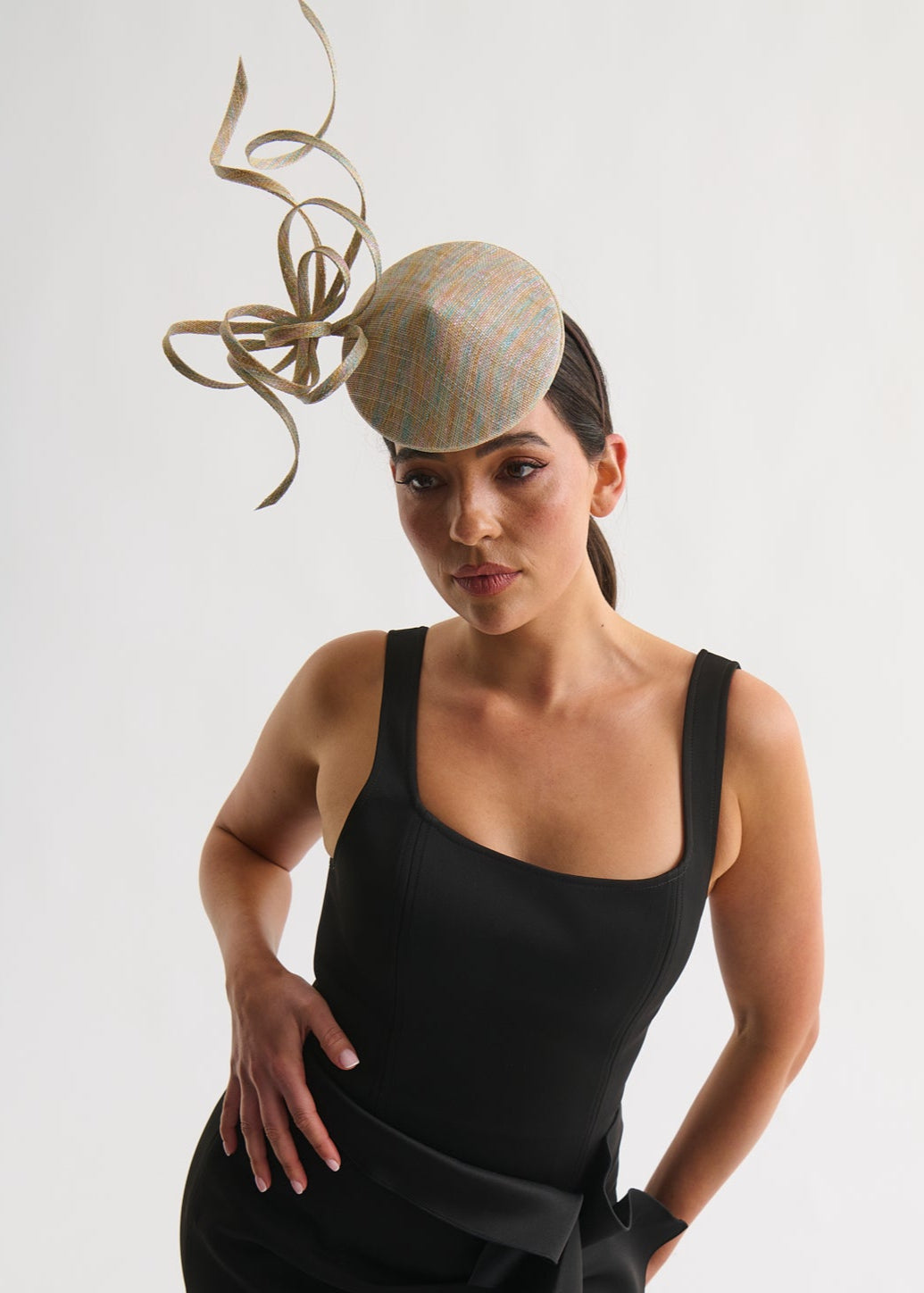 Woman wearing a black dress and a decorative beige hat against a white background