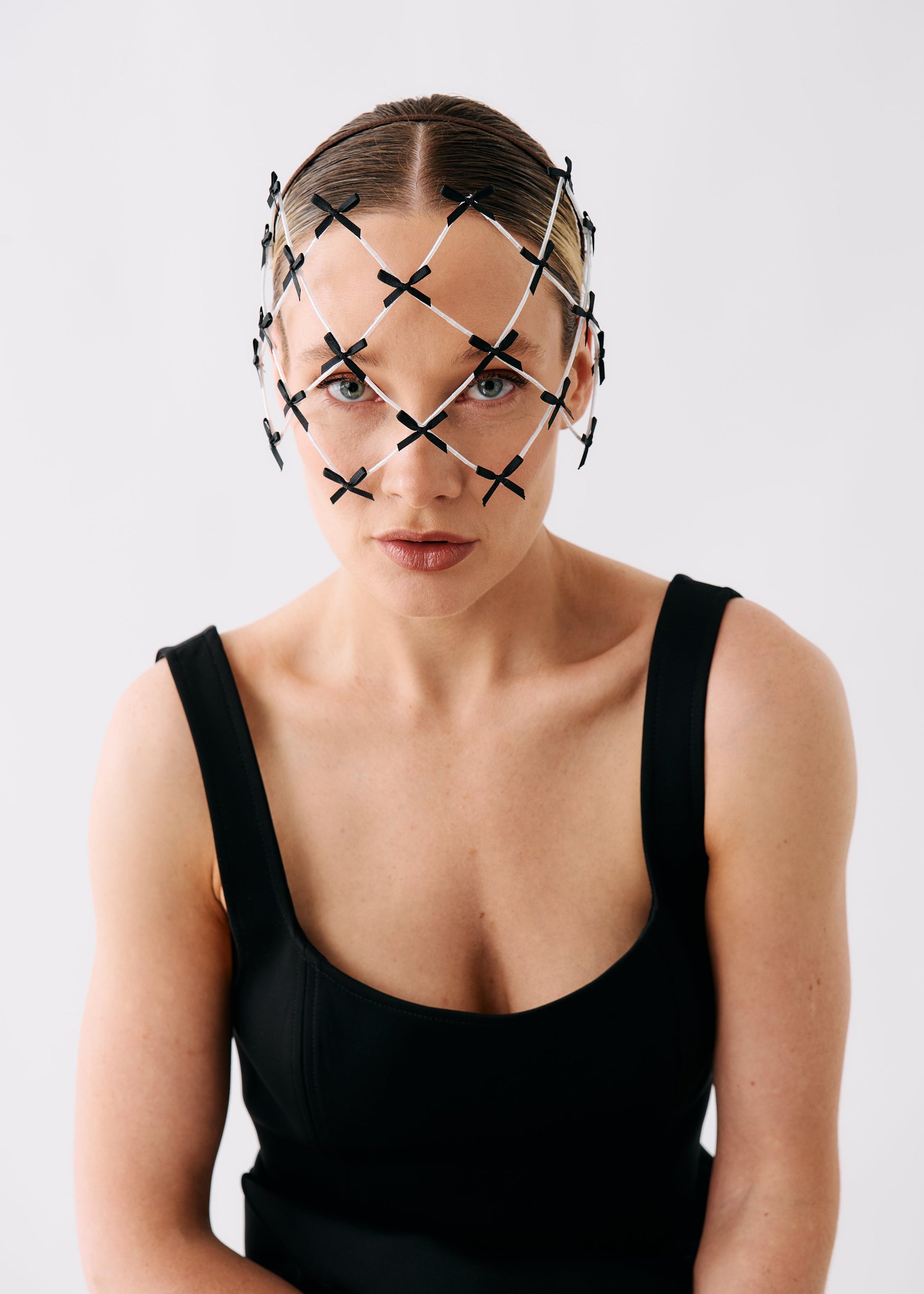 A model wearing a black and white geometric head net with intersecting X-shaped patterns, paired with a black scoop-neck top, set against a plain light gray background.