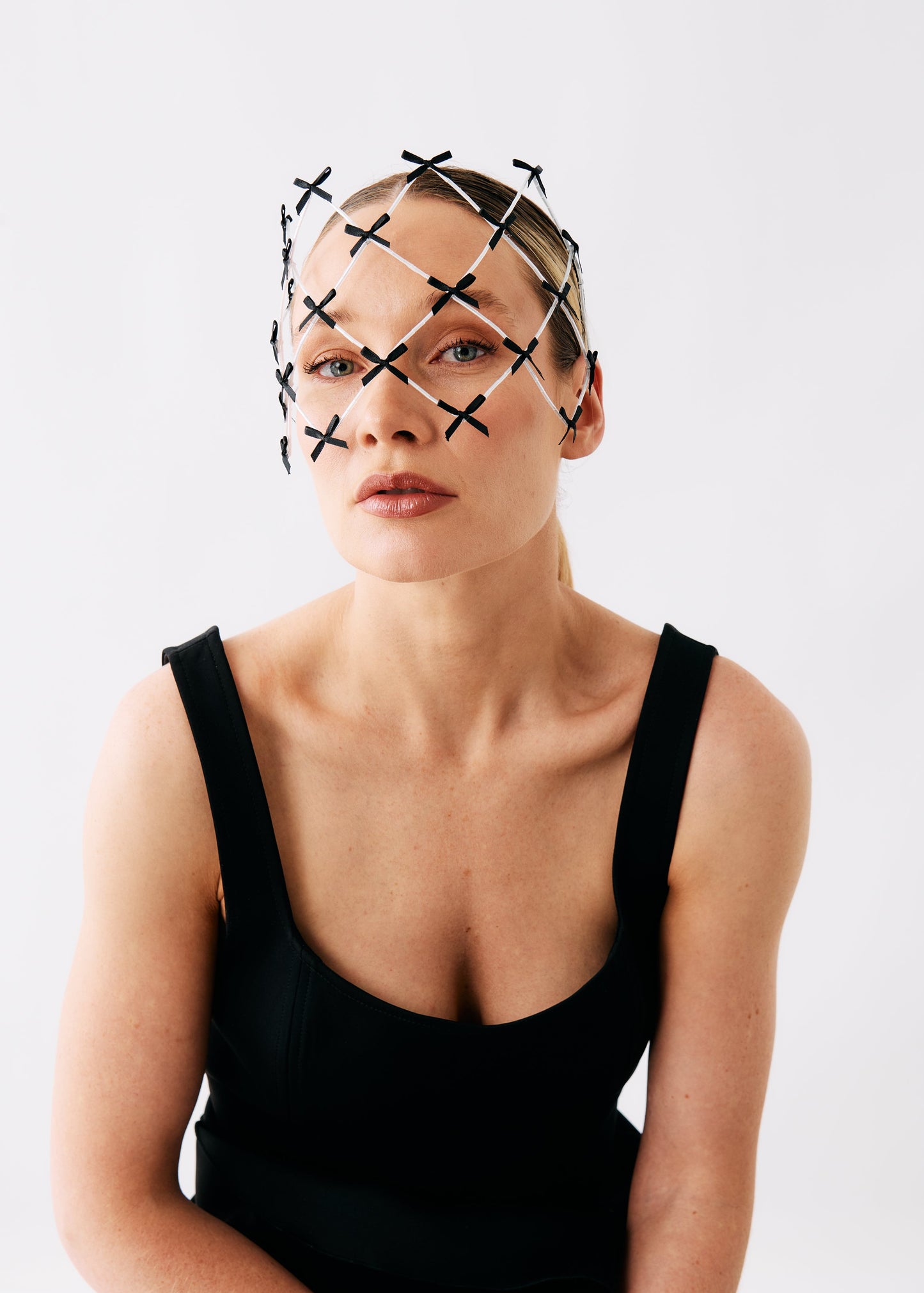 A model wearing a black and white geometric head mesh headband with intersecting X-shaped patterns, paired with a black scoop-neck top, against a plain white studio background.