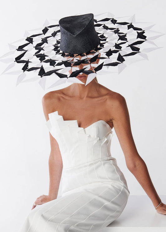 Woman wearing a white strapless dress and a black and white feather brimmed hat on a white background