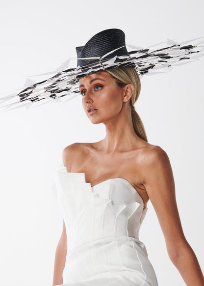 Woman wearing a strapless white dress and black hat with a feather brimmed hat on a white background