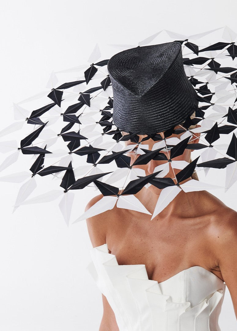 Person wearing a black hat with a geometric feathers on a white background