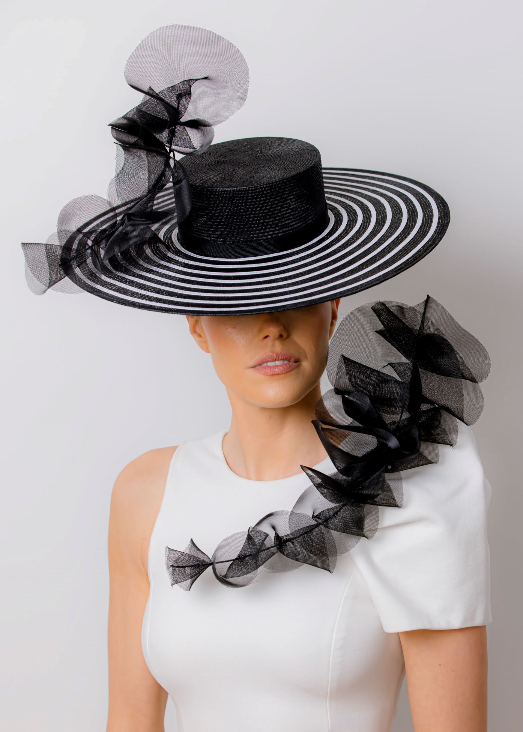 Woman wearing a black and white strip boater hat on a plain background