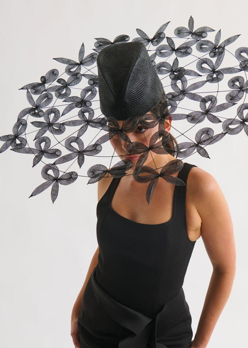 Woman wearing a black dress and hat with bows against a white background