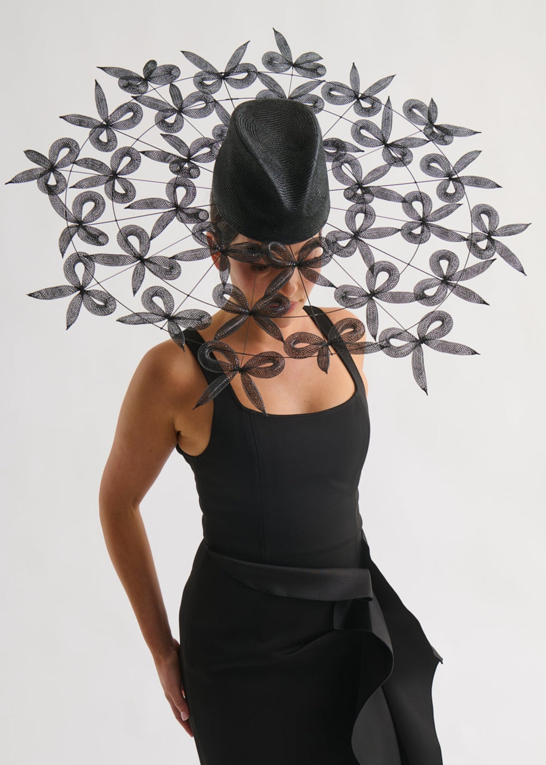 woman wearing a large bow brimmed hat and black dress against a white background.
