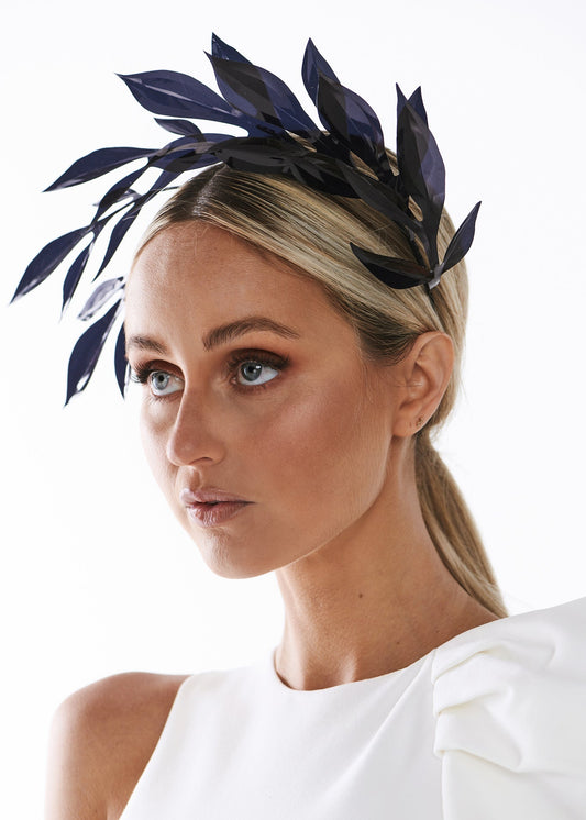 Woman wearing a white dress with a black leaf headpiece against a white background