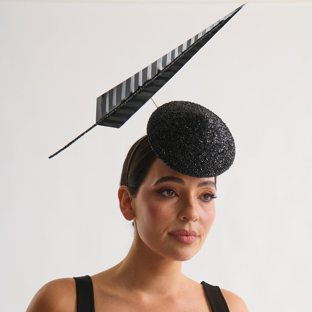 Woman wearing a black dress and decorative hat with a feather against a white background
