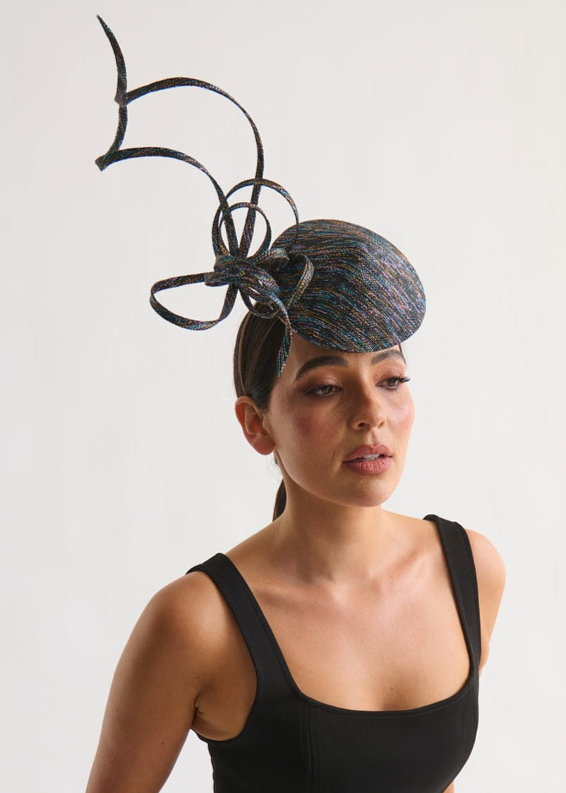 Woman wearing a black dress with a large decorative headpiece against a white background