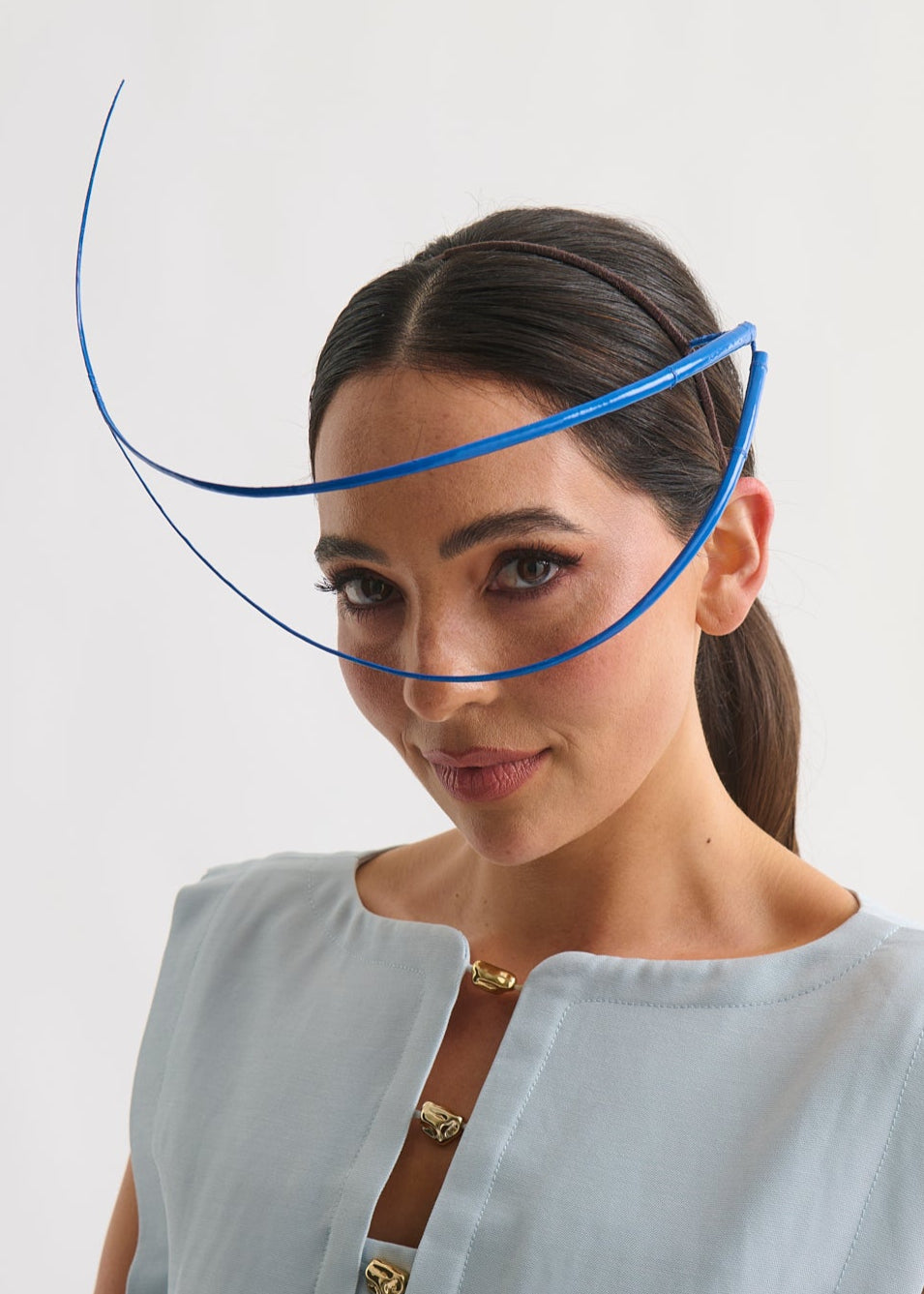 Woman wearing a blue feather quill headpiece and a blue dress against a white background