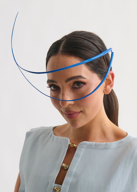 Woman wearing a blue feather quill headpiece and a blue dress against a white background