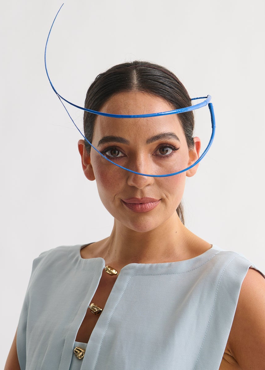 Woman wearing a blue feather quill headpiece and a blue dress against a white background