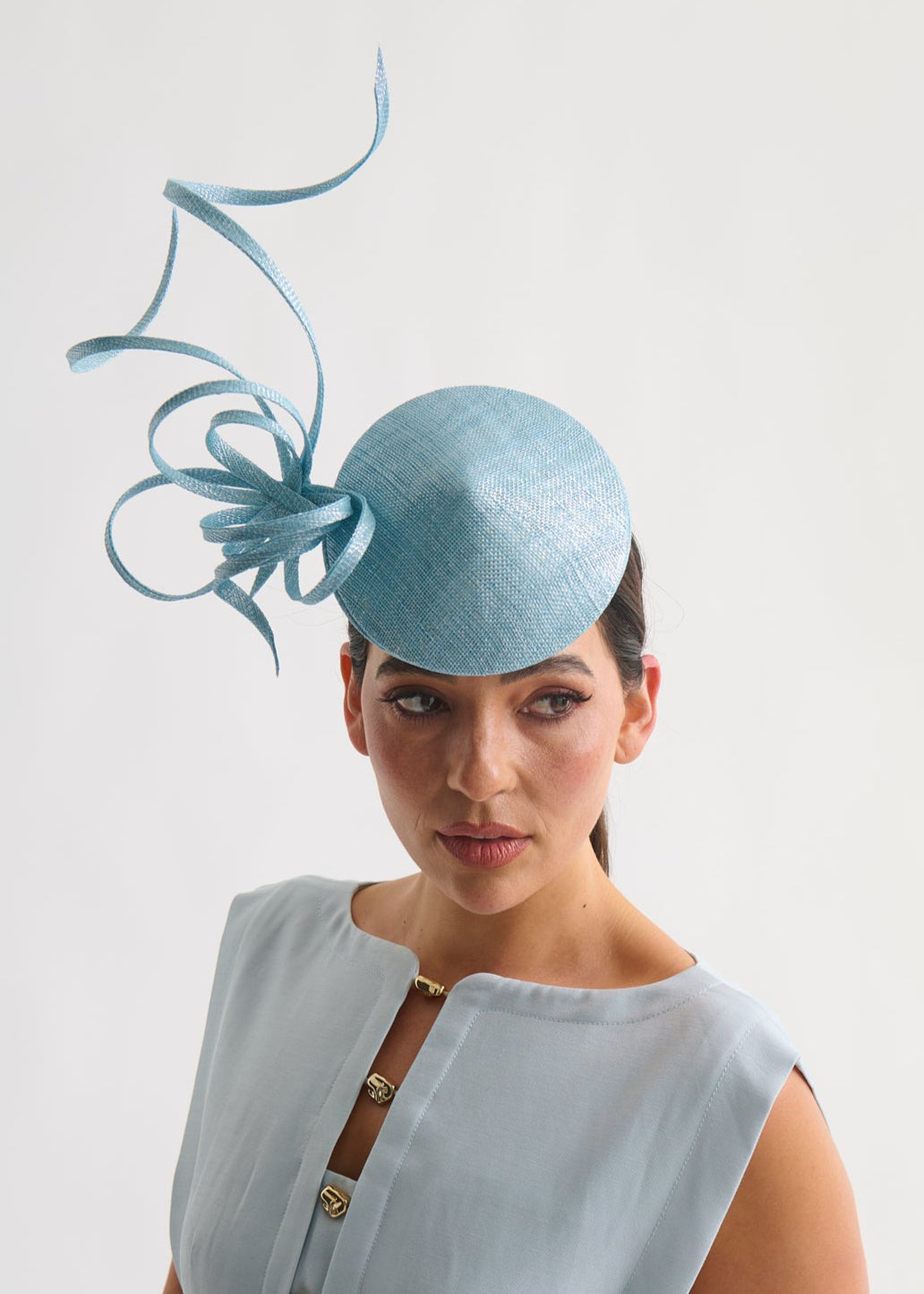 Woman wearing a light blue dress with a matching fascinator on a white background
