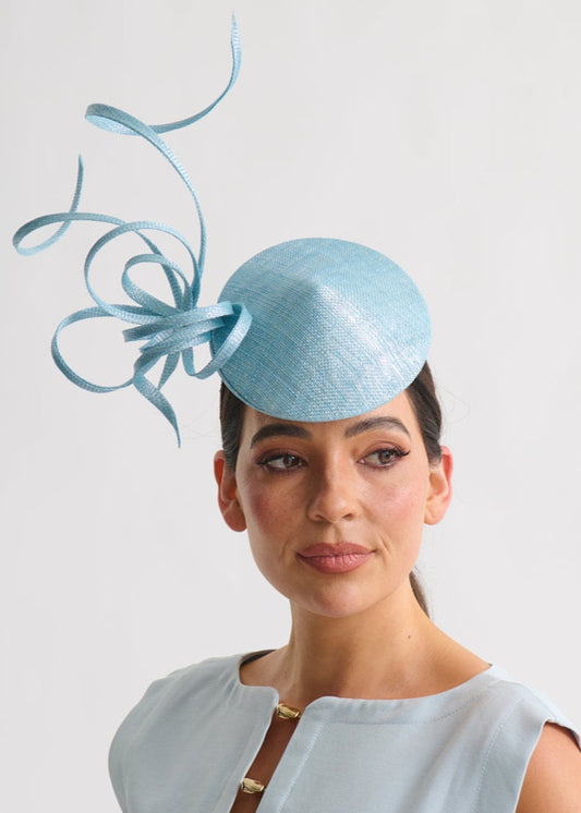 Woman wearing a light blue dress with a matching fascinator against a white background