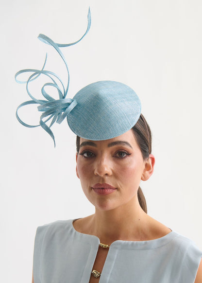 Woman wearing a light blue fascinator with decorative elements on a white background