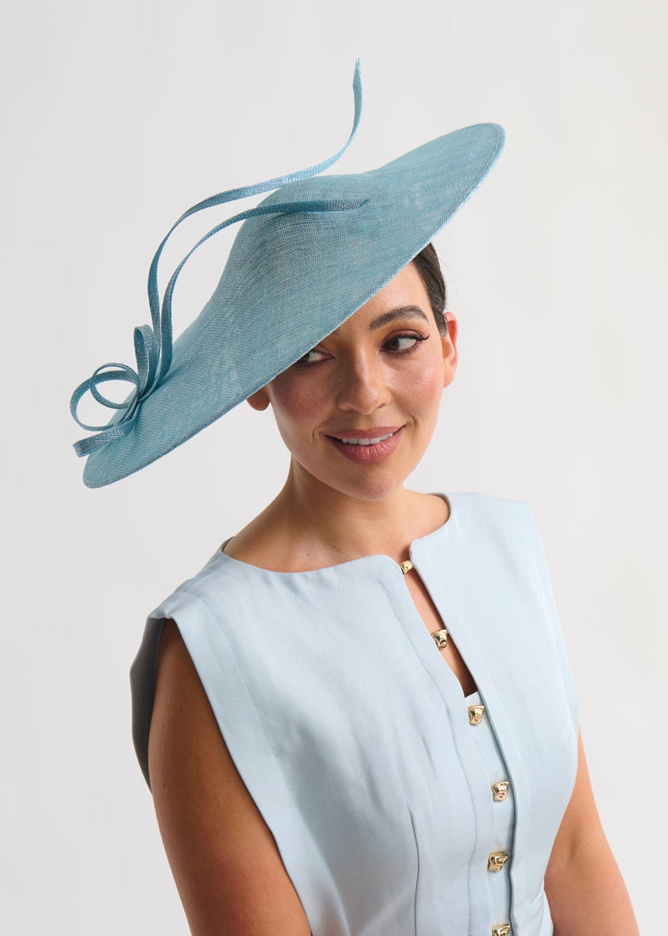 Woman wearing a light blue dress with gold buttons and a matching hat on a white background