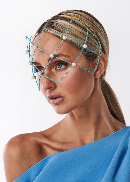 Woman wearing a blue off-shoulder top with a beaded geometric headpiece against a white background