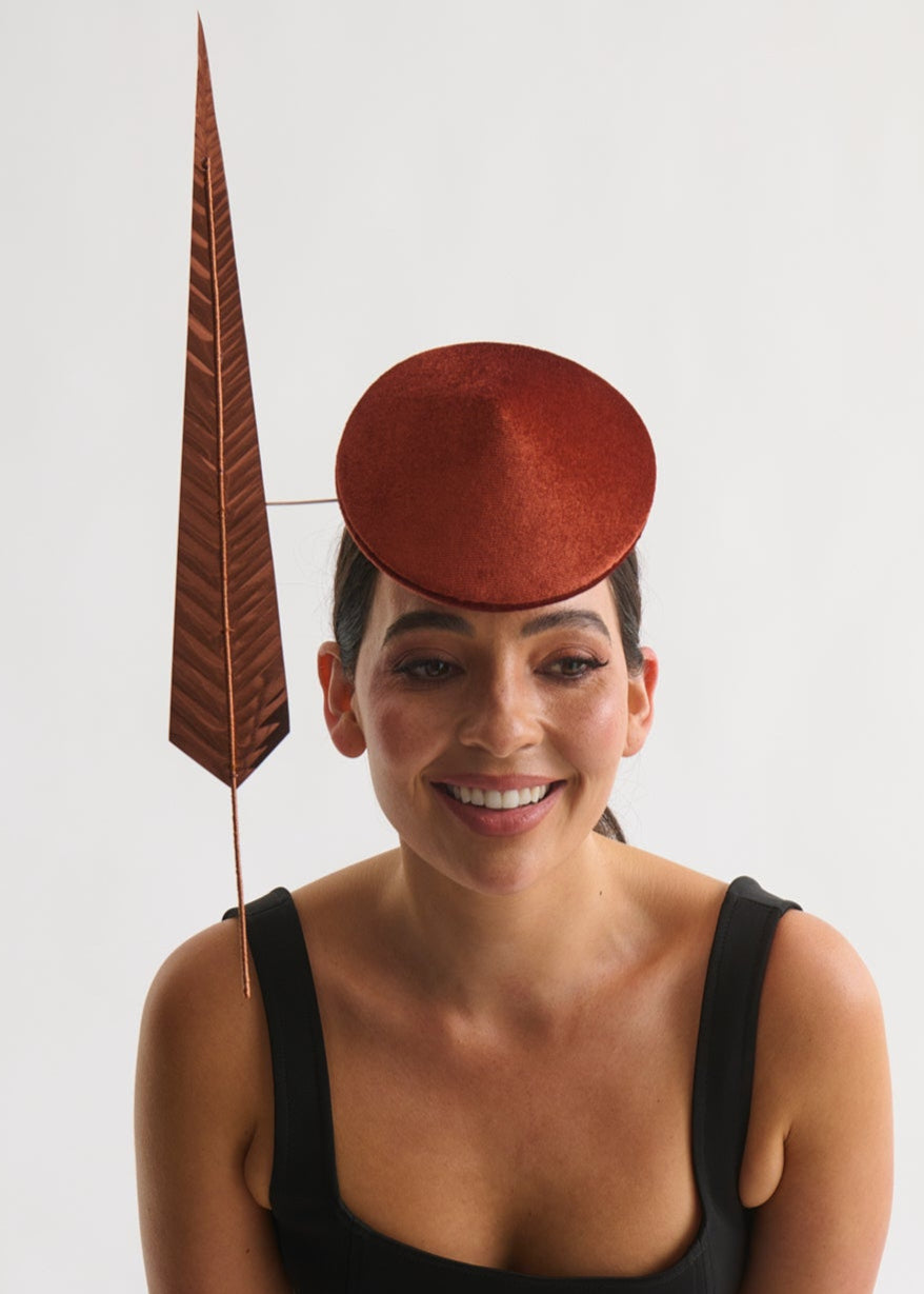 Woman wearing a black dress and copper hat with a feather against a white background