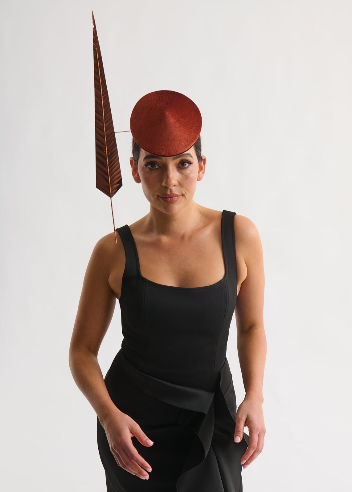 Woman wearing a black dress and a distinctive copper hat with a tall feather on a white background
