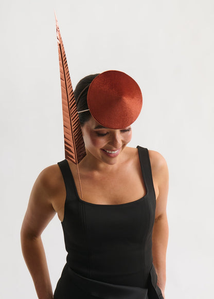 Woman wearing a copper hat with a feather, against a white background