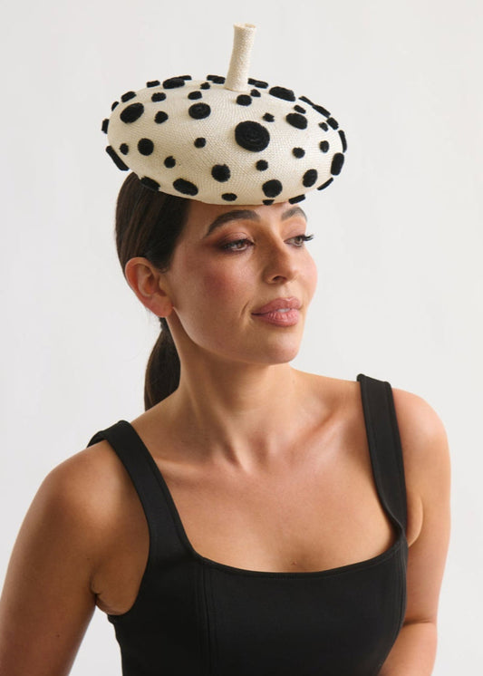 Woman wearing a black and white polka dot headpiece against a plain background