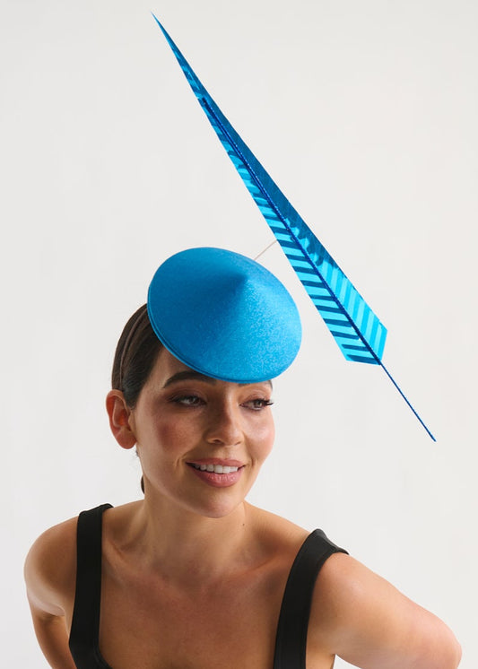 Woman wearing a blue fascinator with a feather on a white background