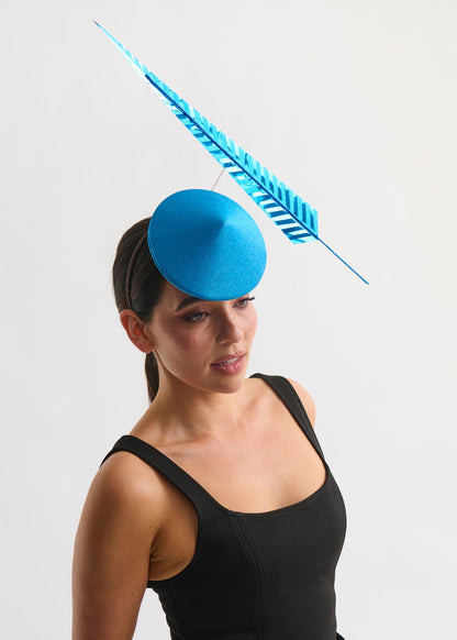 Woman wearing a blue fascinator with a feather on a white background