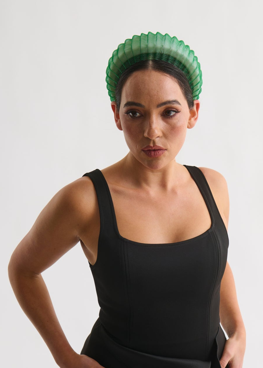Woman wearing a black dress with a green headpiece against a white background