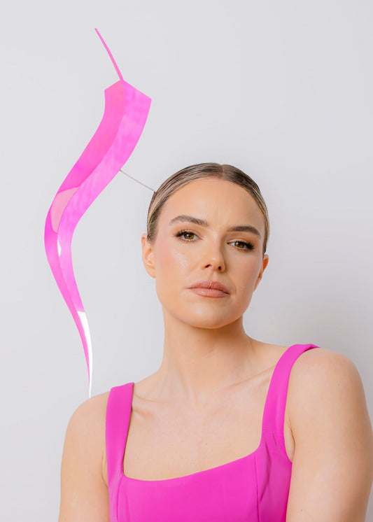 Woman wearing a bright pink dress with a feather headpiece on a light gray background