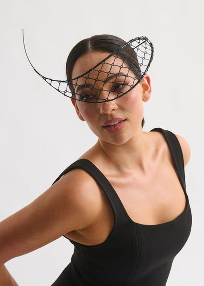 Woman wearing a black sleeveless top and skirt with a decorative headpiece on a white background