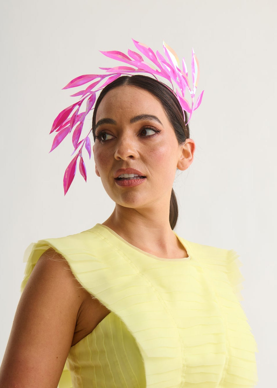 woman wearing a hot pink leaf headpiece and yellow dress with a white background.