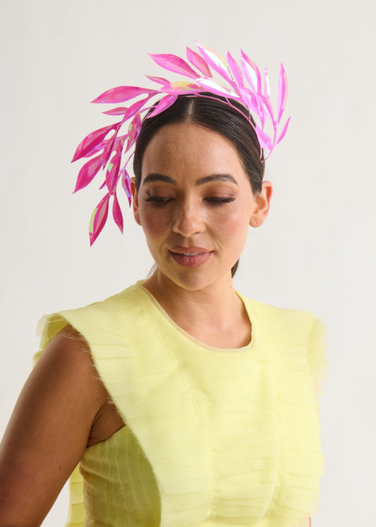 woman wearing a hot pink leaf headpiece and a yellow dress against a white background. 