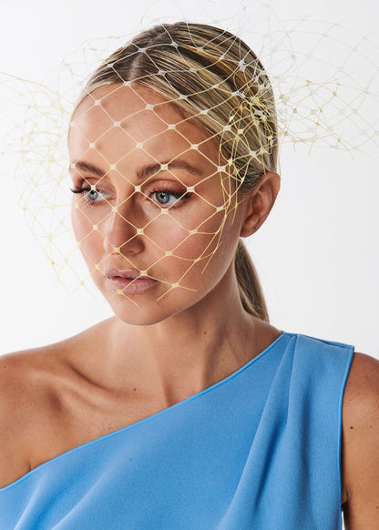 Woman wearing a blue one-shoulder dress with a netting headpiece on a white background