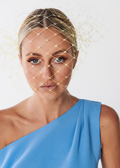 Woman wearing a blue one-shoulder dress with a birdcage veil on a white background