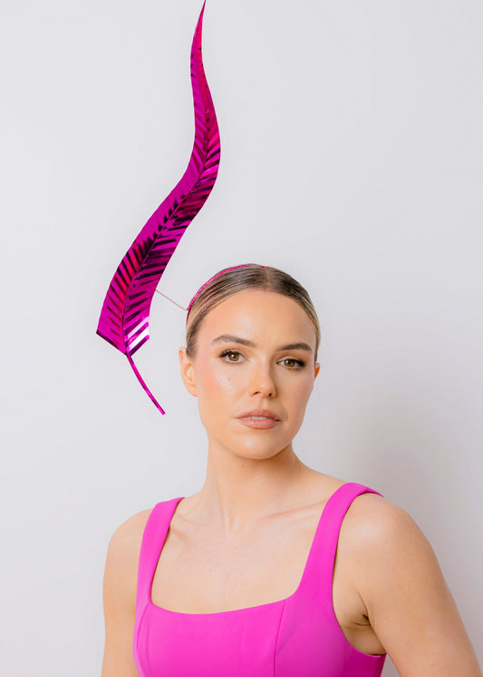 Woman wearing a bright pink dress with a matching feather headpiece against a light background