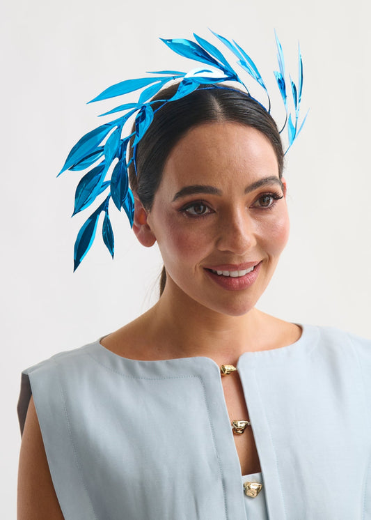 Woman wearing a light blue dress with a decorative headpiece against a white background