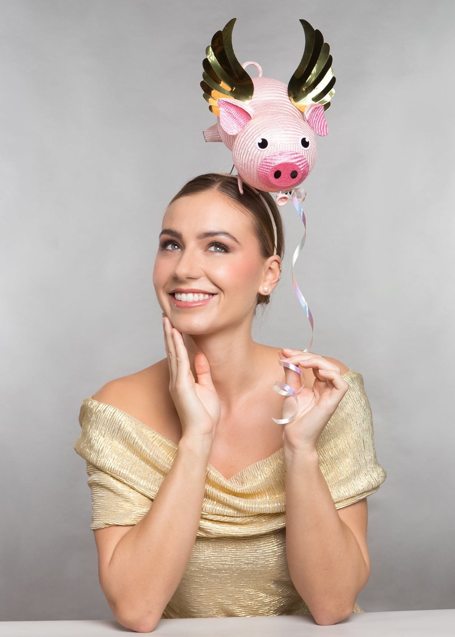 Woman wearing a gold dress with a pink pig hat on a gray background